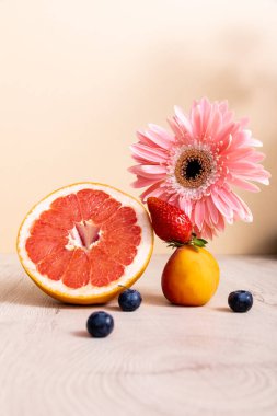Çiçek ve meyve kompozisyonu pembe gerbera, böğürtlen, greyfurt ve kayısı bej üzerine izole edilmiş ahşap yüzey.