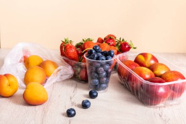 Tahta yüzeydeki plastik kaplarda yaban mersini, çilek, nektarin ve şeftali içeren meyve bileşimi bej rengi.