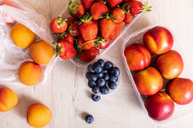Yaban mersini, çilek, nektarin ve şeftali içeren meyve bileşiminin en üst görünümü ahşap yüzey üzerinde plastik kaplarda