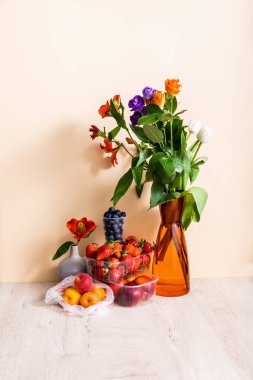 Vazoda çiçek ve meyve kompozisyonu ve bej arka planda ahşap yüzeyde yaz meyveleri.