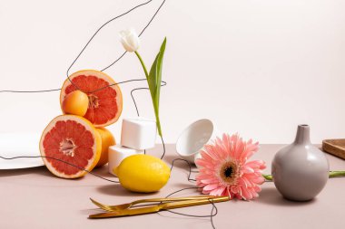 Lale, gerbera, meyve, çatal bıçak, bardak ve vazo içeren çiçek ve meyve kompozisyonu bej üzerine izole edilmiştir.