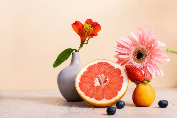 floral and fruit composition with Alstroemeria, gerbera, berries, grapefruit and apricot on wooden surface isolated on beige