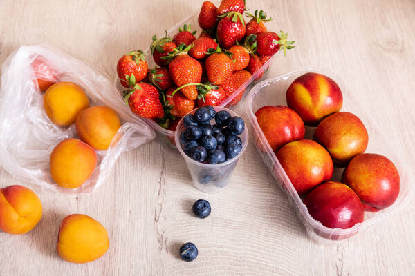fruit composition with blueberries, strawberries, nectarines and peaches in plastic containers on wooden surface