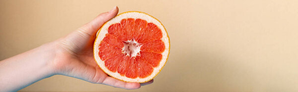 cropped view of female hand with juicy grapefruit half on beige background, panoramic crop