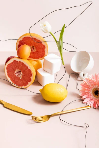 floral and fruit composition with tulip, gerbera, fruits, cutlery, cup isolated on beige