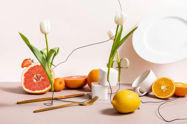 floral and fruit composition with tulips, fruits, dishware isolated on beige
