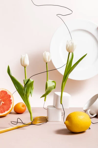 floral and fruit composition with tulips, fruits, dishware isolated on beige