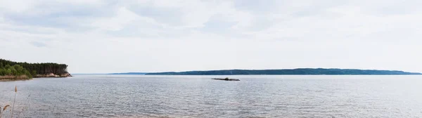 panoramic crop of clean lake near green trees against sky with clouds 