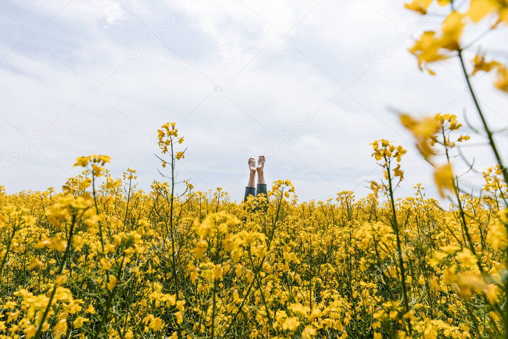 cropped view of barefoot woman near yellow flowers in field against sky 