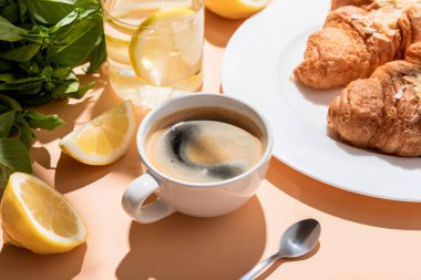 Kahve, kruvasan ve bej masadaki kahvaltıda limonlu bir bardak su.