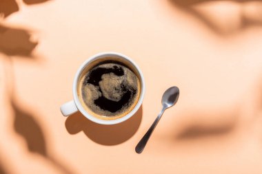Kahve fincanının üst görüntüsü ve gölgeli bej çay kaşığı