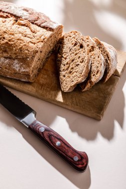Taze pişmiş ve dilimlenmiş ekmek kesme tahtasında, gri masada gölgeli bıçakla.