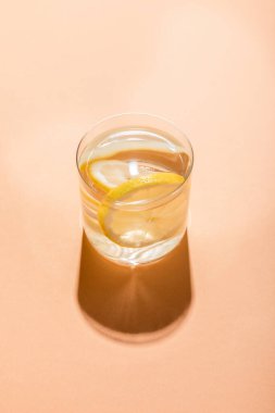 Bir bardak taze su ve limon dilimleri bej üzerine gölge. 