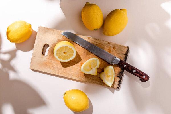 whole and cutted lemons on wooden board with knife on grey table