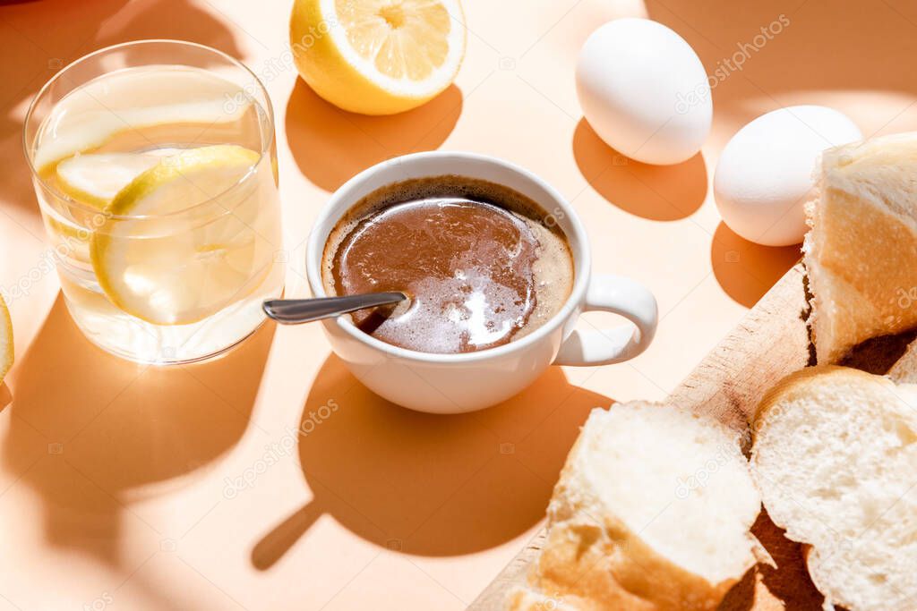 coffee, eggs, baguette and glass of water for breakfast on beige table