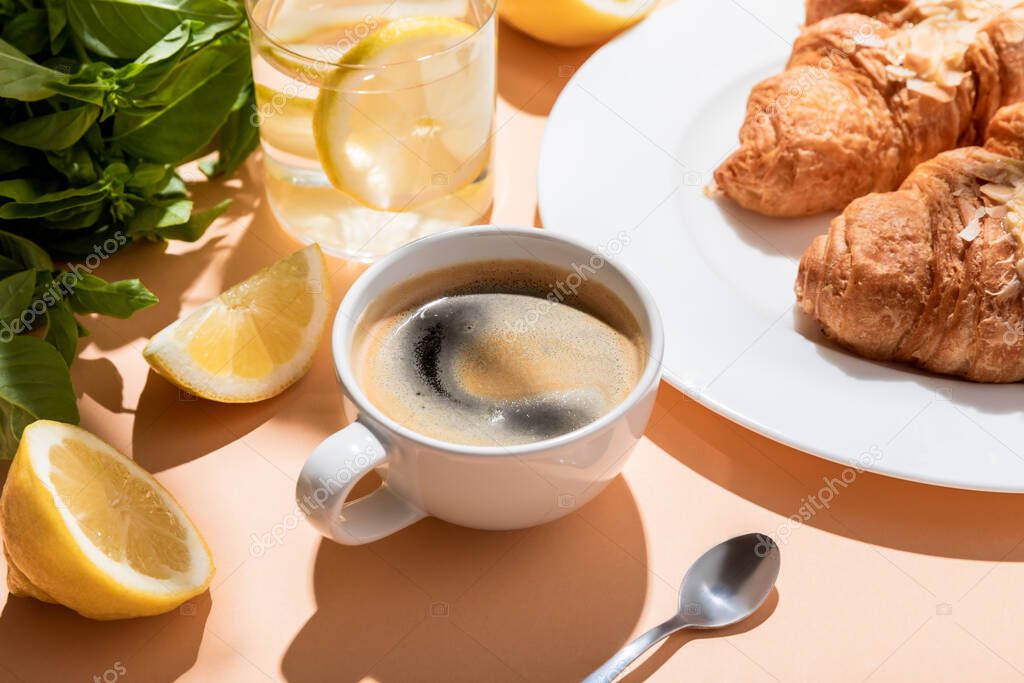 coffee, croissants and glass of water with lemon for breakfast on beige table