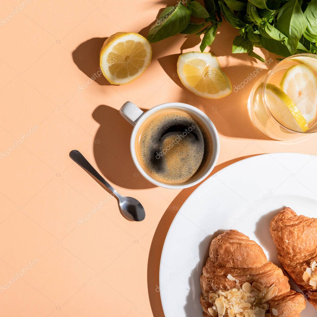 top view of coffee cup, greenery, lemons and croissants for breakfast on beige table