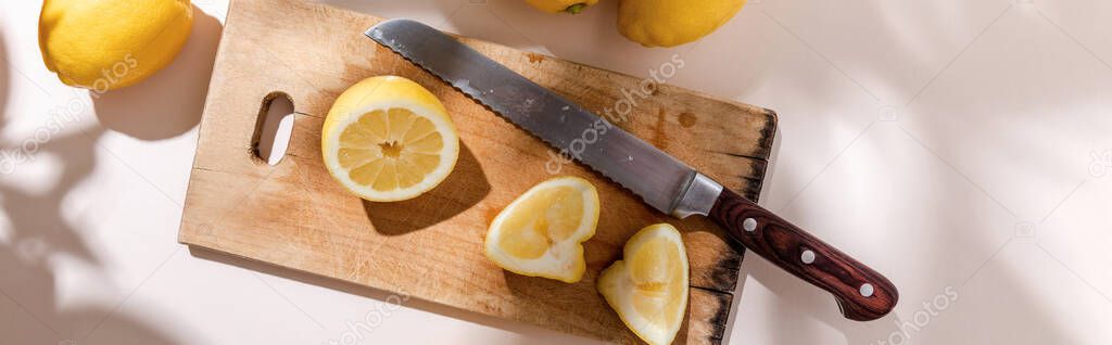 top view of cutted lemons on wooden board with knife on grey table, panoramic concept