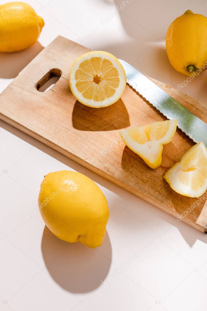 fresh whole and cutted lemons on wooden board with knife on grey table 