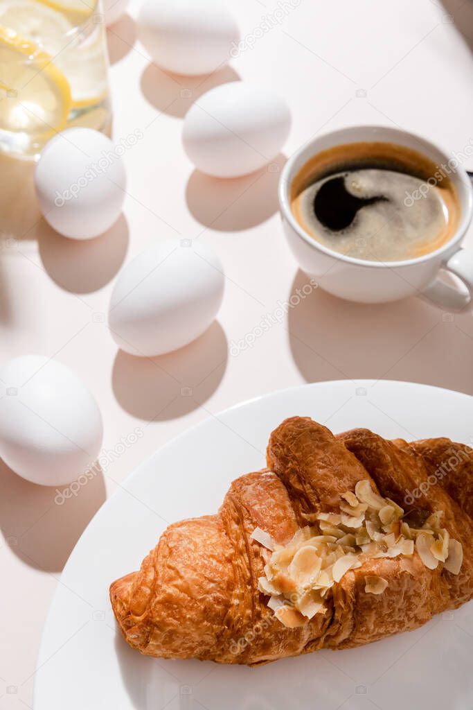 eggs, croissant, coffee and water with lemon for breakfast on grey table with shadows