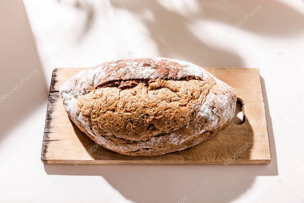 top view of fresh baked bread on wooden board on grey table with shadows