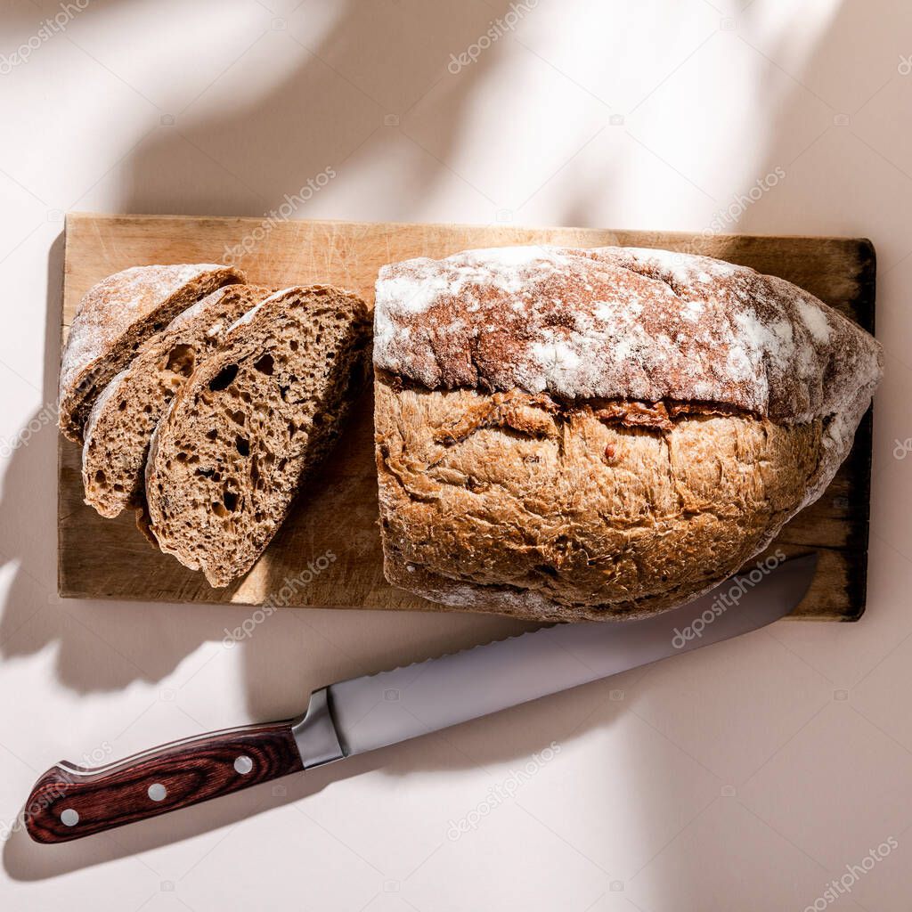 top view of fresh baked and sliced bread on board with knife on grey table with shadows