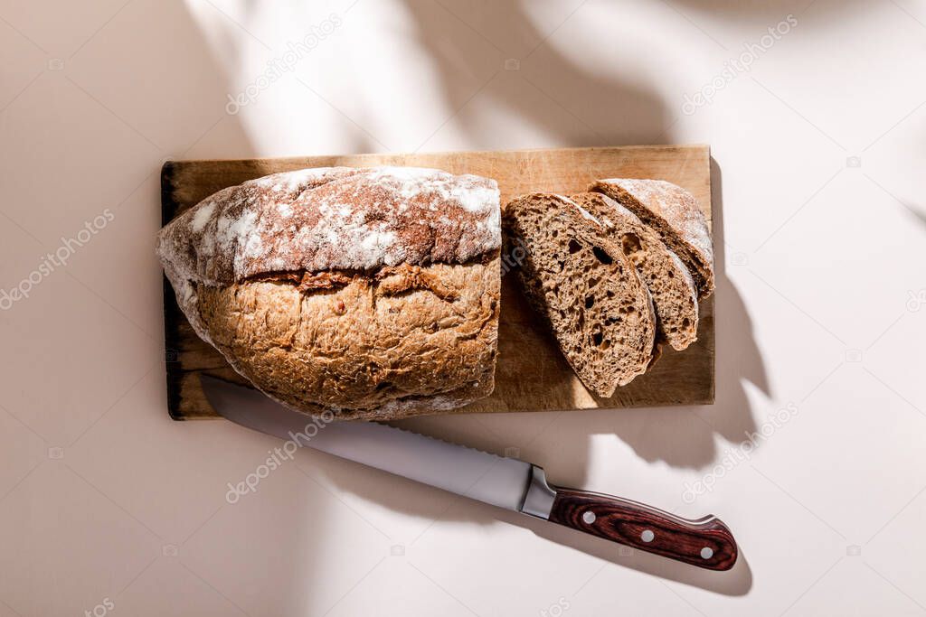 top view of fresh baked and sliced bread on cutting board with knife on grey table with shadows