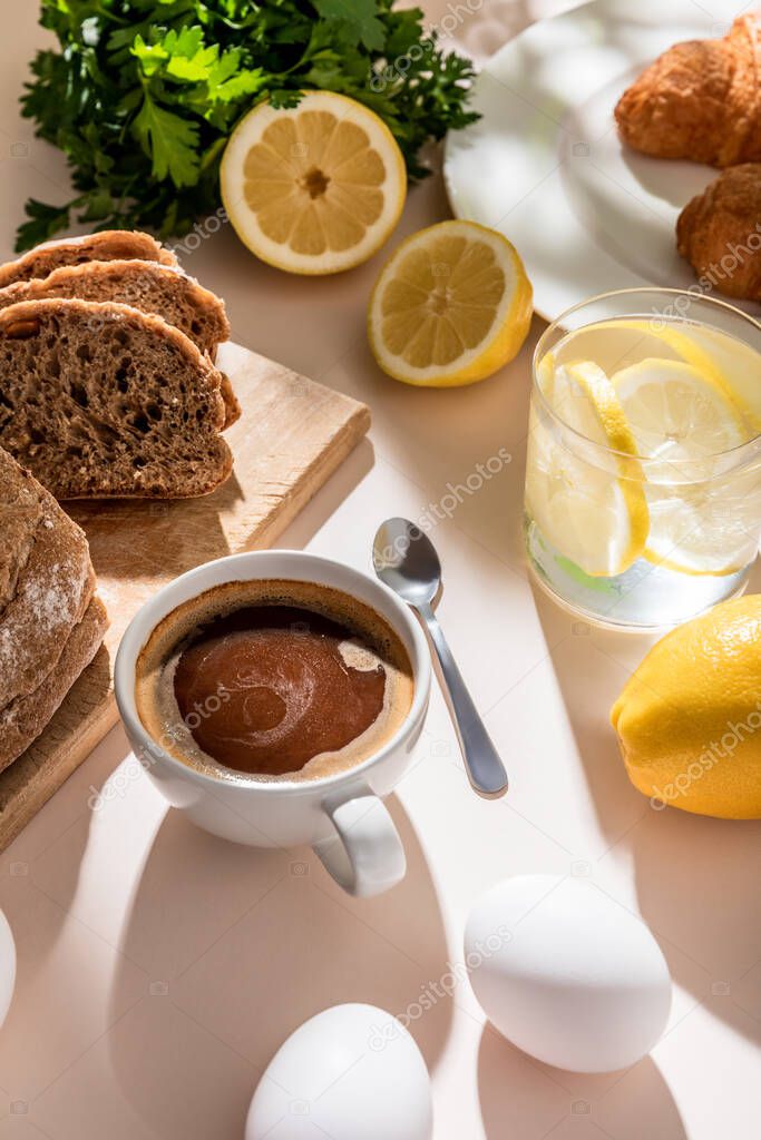 fresh bread, eggs, lemon water and cup of coffee for breakfast on grey table 
