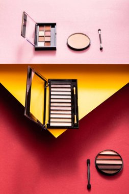 eye shadow palettes and double-sided eyeshadow applicators near face powder on crimson, pink and yellow clipart