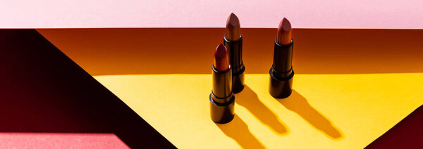 панорамный снимок теней возле помад на желтом и розовом
 