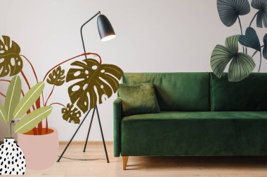 Modern zemin lambası ve çizilmiş bitki resimli yastıklı yeşil kanepe. 