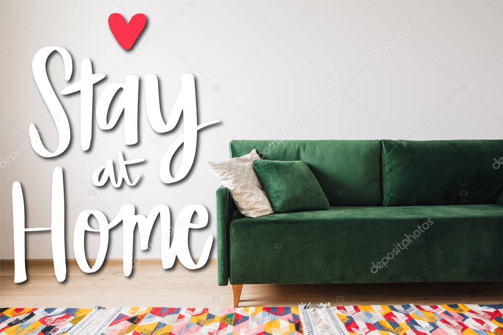 modern green sofa and pillows in living room with colorful rug near stay at home lettering 