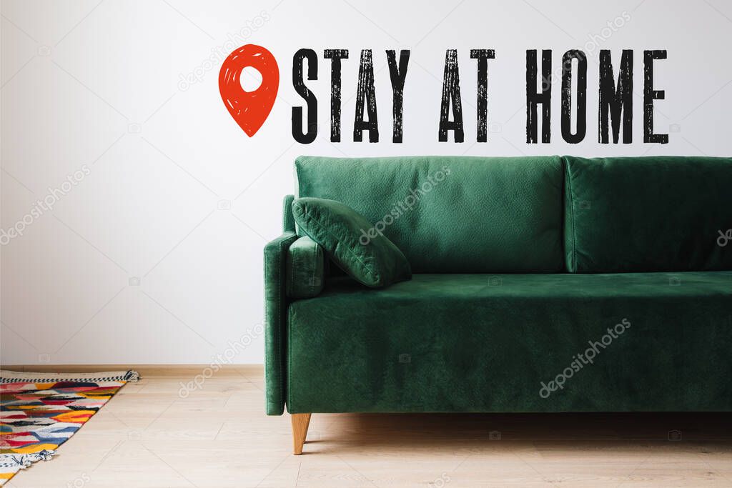green sofa with pillow near colorful rug and stay at home lettering 