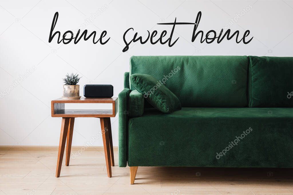 green sofa, pillow, wooden coffee table with plant and alarm clock near home sweet home lettering 