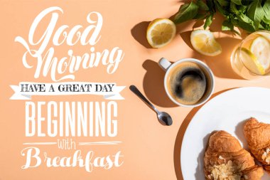Kahvaltı için bej masadaki kahve ve kruvasan manzarası. İyi sabahlar. Kahvaltı harfleriyle başlıyor.