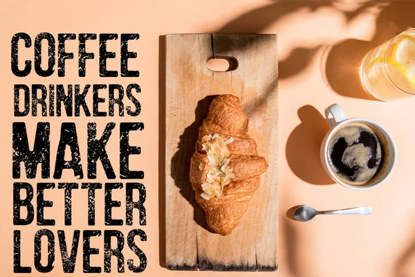 top view of coffee, water and croissant on wooden board for breakfast on beige table with coffee drinkers make better lovers lettering