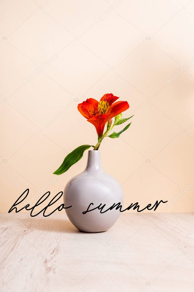 red Alstroemeria in vase on wooden surface near hello summer lettering on beige