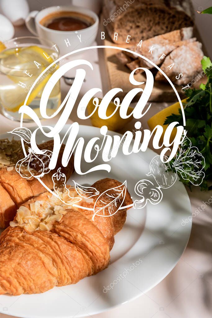 fresh croissants, bread, coffee and lemon water on grey table, selective focus with healthy breakfast, good morning lettering