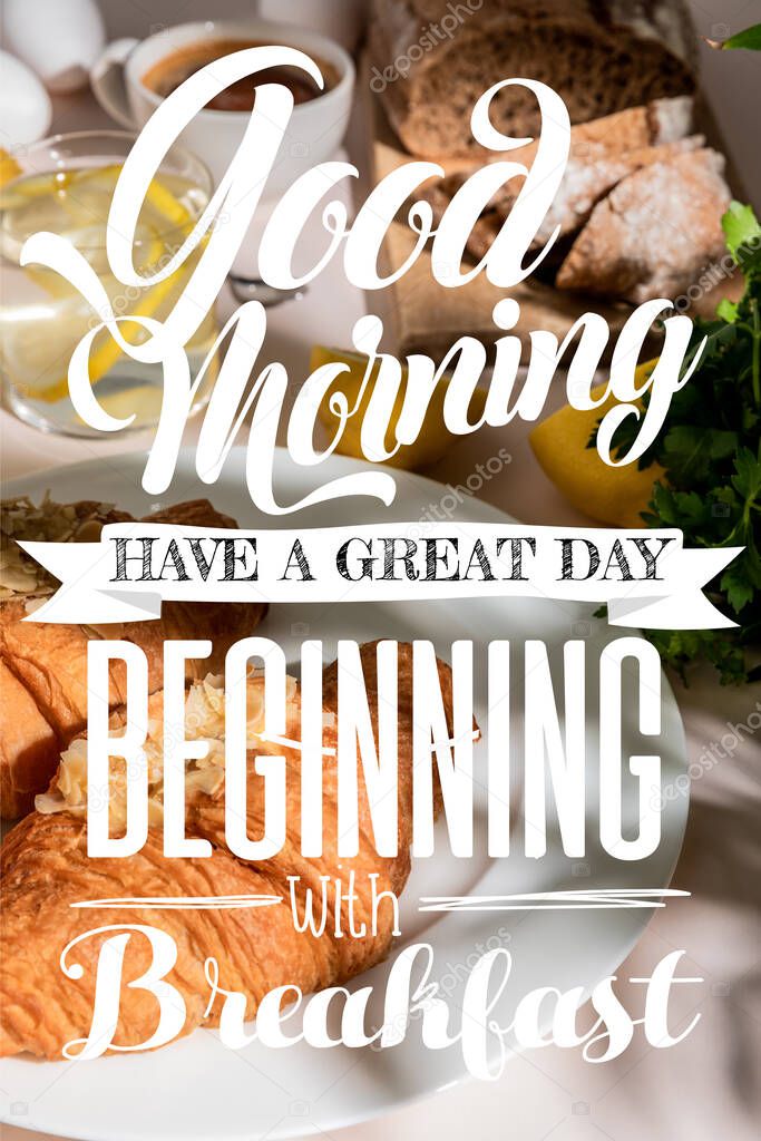 fresh croissants, bread, coffee and lemon water on grey table, selective focus with good morning, have a great day, beginning with breakfast lettering