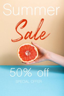 cropped view of woman holding juicy half of grapefruit near summer sale, fifty percent off, special offer lettering on beige and blue  clipart