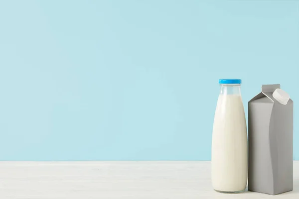 Imagen de primer plano de la leche en botella y el paquete de cartón en blanco sobre fondo azul - foto de stock