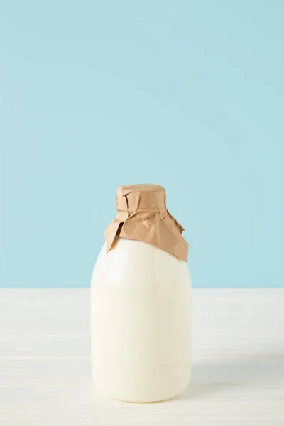 Vista de cerca de la leche fresca en botella envuelta por papel sobre fondo azul - foto de stock
