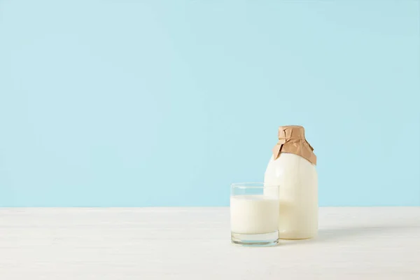 Vaso de leche y leche en botella envueltos en papel sobre fondo azul - foto de stock