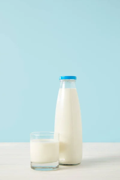 Vista de primer plano de botella de leche y vaso de leche sobre fondo azul - foto de stock