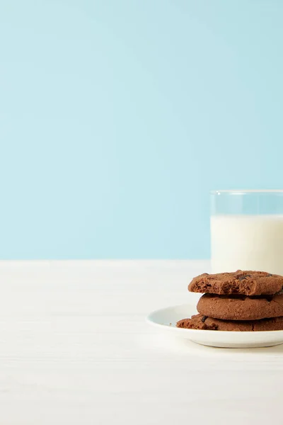 Biscotti al cioccolato sul piattino e vetro del latte su sfondo blu — Foto stock