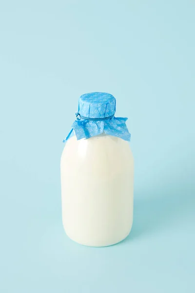 Nahaufnahme von frischer Milch in Flasche, umwickelt mit Papier auf blauem Hintergrund — Stockfoto