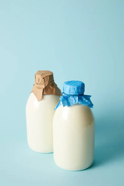 Deux bouteilles de lait frais enveloppées par du papier sur fond bleu — Photo de stock