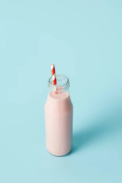 Closeup view of strawberry milkshake in bottle with drinking straw on blue background — Stock Photo