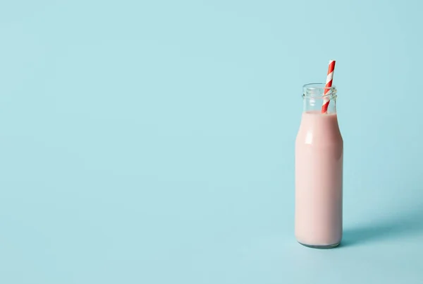 Erdbeer-Milchshake in Flasche mit Trinkhalm auf blauem Hintergrund — Stockfoto