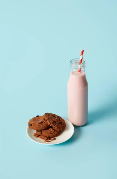 Biscoitos de chocolate em pires e batido de morango em garrafa com palha de bebida no fundo azul — Fotografia de Stock